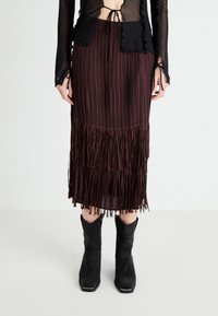 Fustă plisată burgundă cu detalii din franjuri la margine, asortată cu cizme negre până la gleznă. Fabricată dintr-un material texturat, având talie ajustată.