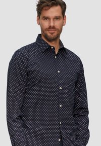 Donkerblauw shirt van katoen met een geometrisch patroon in het wit en rood. Heeft een button-down kraag en knopen aan de voorkant. Lange mouwen.