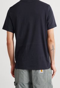 Tmavě modré bavlněné tričko s krátkými rukávy a kulatým výstřihem, s štítkem na dolní levé straně. Materiál vypadá hladce.