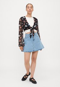 Fekete áttetsző crop top színes ajakmintával, deréknál megkötve. Világoskék farmer A-vonalú szoknyával és fekete lapostalpú cipővel párosítva.