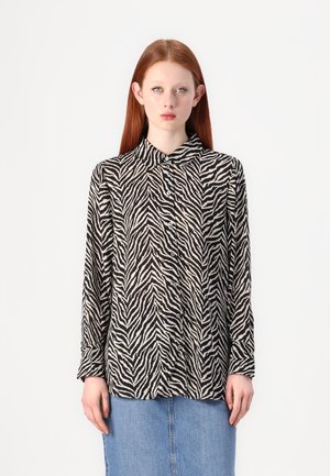 Black and white zebra print long-sleeve shirt with a collared neckline and buttons, made from a lightweight fabric. Styled with a denim skirt.
