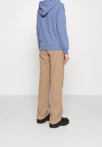 Modrá mikina s kapucí, béžové manšestrové kalhoty a černé masivní boty. Ležérní styl s měkkými texturami, viditelnými švy a volnou siluetou.