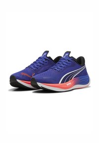 Zapatillas de running Puma con una parte superior de malla morada transpirable, detalles negros, suela blanca y rosa, y detalles reflectantes en los laterales.