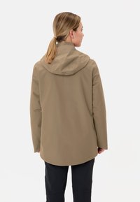 Giacca impermeabile marrone con cappuccio, texture liscia e taglio lungo, mostrata da dietro, abbinata a pantaloni neri.