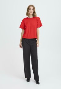 Top rojo de manga corta con escote redondo, combinado con pantalones negros a medida, de pierna ancha, y tacones negros, sobre un fondo neutro.