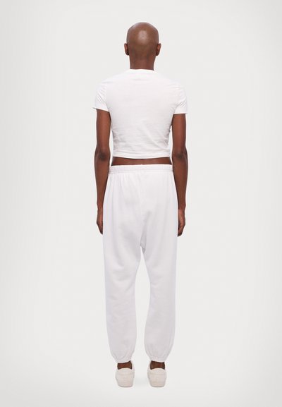 T-shirt blanc court et joggers blancs avec des poignets élastiques, présentés de dos. Le tissu semble doux et lisse. Tenue décontractée.