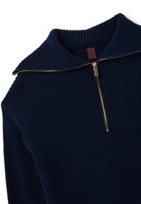 Pull en maille bleu marine avec un motif texturé, doté d'un grand col et d'une fermeture éclair dorée à l'avant. Étiquette visible au niveau du col.