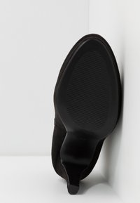 Chaussure à talons hauts en daim noir avec un bout pointu et une semelle lisse et incurvée présentant une texture striée pour une meilleure adhérence.