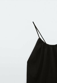 Haut sans manches noir avec de fines bretelles, décolleté froncé et délicate bordure festonnée le long des bords. Tissu léger avec une légère texture.