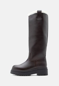 Botă maro din piele, până la genunchi, cu o finisare texturată, căptușeală din blană artificială albă la vârf și talpă din cauciuc negru, robustă.