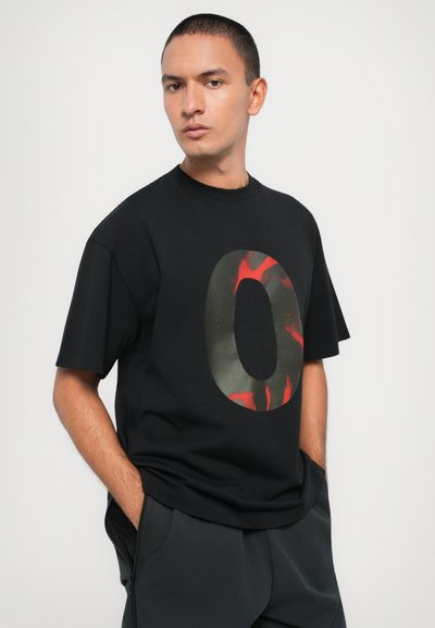 Black t-shirt with short sleeves and a large graphic "O" printed in green and red. Soft material, relaxed fit, rounded neck.