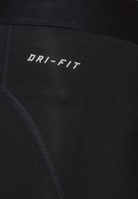 Gros plan sur un tissu noir avec des coutures visibles et le texte blanc "DRI-FIT" imprimé à la surface.