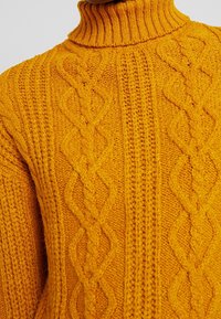 Kabelstrick-Turtleneck-Pullover in leuchtendem Gelb. Mit strukturierten Mustern und geripptem Kragen. Hergestellt aus einem weichen, dicken Stoff.
