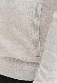 Jasnoszara bluza z miękką fakturą, z prążkowanymi akcentami na dole i przy bocznej kieszeni. Widoczne subtelne różnice w odcieniu.