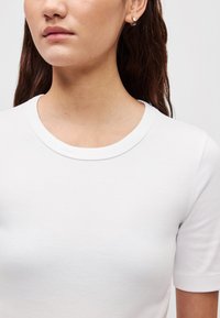 Λευκό βαμβακερό μπλουζάκι με στρογγυλή λαιμόκοψη και κοντά μανίκια, με απαλή υφή και εφαρμοστή γραμμή. Απλός �και λιτός σχεδιασμός.