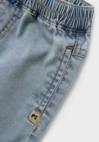 Shorts in denim azzurro chiaro con vita elasticizzata, tasche laterali e una piccola etichetta in pelle marrone vicino alla cucitura. Dettagli di texture e cuciture sottili.