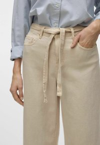 Beiga vida byxor i lätt material, med knytbar midja och framfickor. Kombinerat med en ljusblå button-up skjorta.