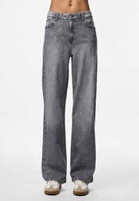 Plati gaisie džinsi, izgatavoti no denima, ar vidēju jostas augstumu, klasisko piecu kabatu dizainu un nedaudz izbalējušu izskatu. Apvienoti ar ikdienišķām sporta apaviem.