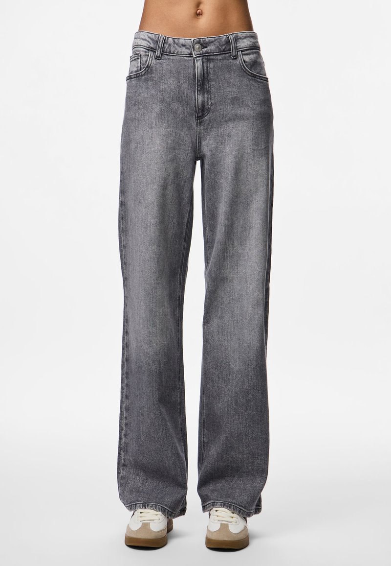 Plati gaisie džinsi, izgatavoti no denima, ar vidēju jostas augstumu, klasisko piecu kabatu dizainu un nedaudz izbalējušu izskatu. Apvienoti ar ikdienišķām sporta apaviem.