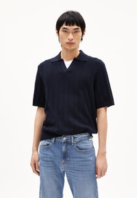 Marine gebreide poloshirt met korte mouwen en verticale geribbelde textuur en een V-hals, gecombineerd met lichtblauwe spijkerbroek.