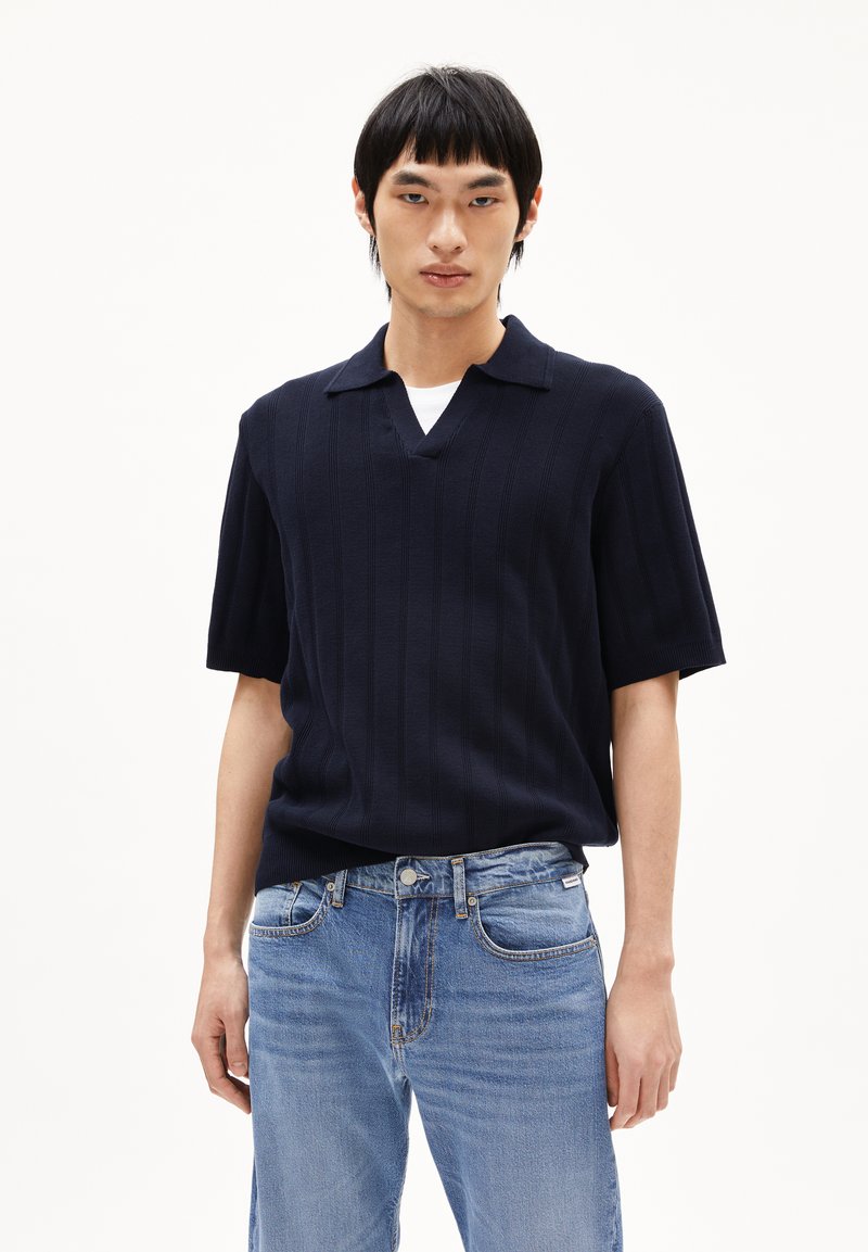 Marine gebreide poloshirt met korte mouwen en verticale geribbelde textuur en een V-hals, gecombineerd met lichtblauwe spijkerbroek.