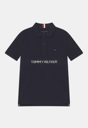 Polo bleu marine à manches courtes, patte de boutonnage à deux boutons, petit logo drapeau Tommy Hilfiger sur la poitrine et nom de la marque blanc sur le devant.