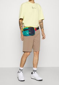 Barevná ledvinka se zipem, která má tyrkysové, námořnické a žluté panely. Nosit ji s lehkým žlutým tričkem a béžovými šortkami.