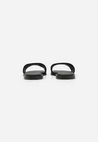 Black slide sandals with open design, flat sole, and smooth texture. Features rounded straps and minimalistic branding on the side.