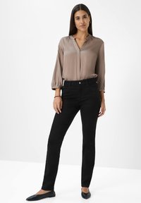 Blusa de tafetán taupe con escote en V y mangas fruncidas, combinada con jeans negros ajustados y bailarinas negras. Diseño minimalista y ajuste estilizado.