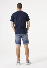 Camiseta azul marino de manga corta, usada con shorts de mezclilla arremangados. Las zapatillas tienen acentos en azul. Diseño sencillo, estilo casual.