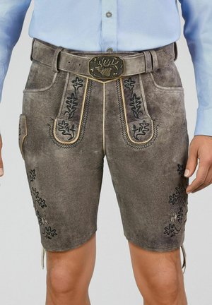 Mann trägt traditionelle braune Lederhosen mit bestickten Blumenmustern und einem Gürtel mit einer Hirschkopf-Schnalle.