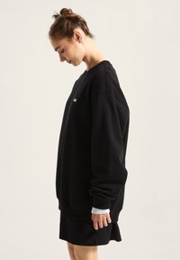 Black sweatshirt with long sleeves, crew neckline, and a loose fit, featuring a gray textured cuff at the wrists. Simple logo detail on chest.