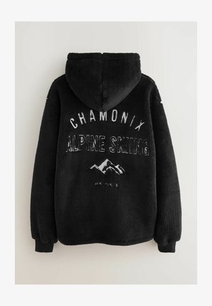 Musta kapuutsiga fliisjakk, millel on tekstuuriga välimus, millel on valge tikitud tekst "CHAMONIX ALPINE SKIING" ja mägi graafika.