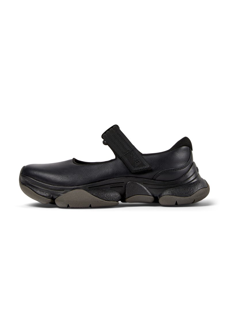 Chaussure de style Mary Jane noire avec semelle épaisse et segmentée et sangle Velcro réglable sur le coup de pied, présentée en profil latéral sur fond blanc.