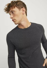 Camisa de punto de manga larga de color gris oscuro con un patrón texturizado y escote redondeado, que presenta mangas raglán y un diseño ajustado.