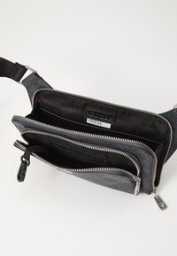 Sac bandoulière en tissu gris avec deux compartiments zippés, quincaillerie en métal argenté, texture lisse et doublure intérieure avec logo.
