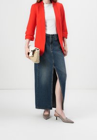 Czerwony żakiet, biały top, spódnica maxi z wysokim stanem z dżinsu z rozporkiem z przodu, beżowe szpilki w szpic oraz mała pleciona torebka.