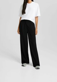 Vit oversized t-shirt i kombination med högmidjade, vida svarta byxor och grå sneakers. Tyget verkar vara mjukt med en avslappnad passform.