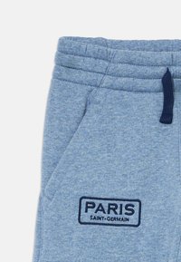 Svetlo modri trenirčki z elastičnim pasom, stranskim žepom, temno modrim vrvico in vezenim značko "PARIS SAINT-GERMAIN" na nogi.