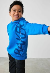 Blauwe hoodie gemaakt van zachte stof, met een grote graphic in donkerblauw, tekst aan de zijkant en een buidelzak. Zwarte cargo broek.
