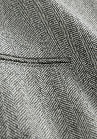 Tissu à chevrons gris avec un tissage texturé et un éclat subtil, présentant un détail de couture lisse le long d'un bord.