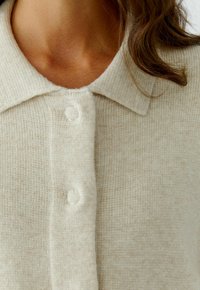 Beige geribde brei cardigan met een vlakke kraag en twee knopen, met een zachte textuur en een subtiel gestructureerd patroon.