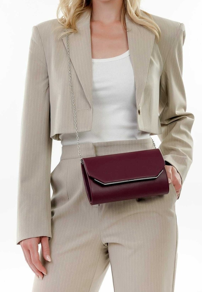 Sac bandoulière en similicuir bordeaux avec fermoir à rabat et ferrures argentées, présentant une forme cylindrique élégante et une texture lisse.