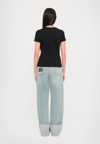 Svart kortermet t-skjorte sammen med vide lyseblå denimjeans som har et særpreget baklommelys design.
