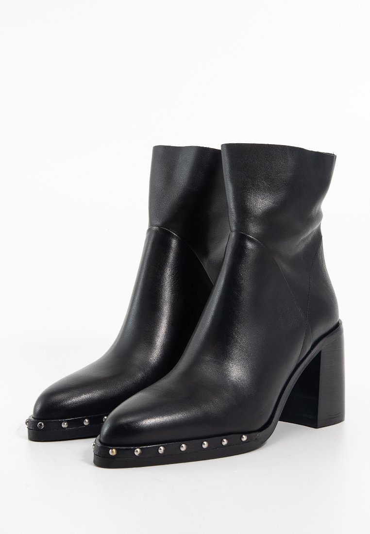 Schwarze Leder-Stiefeletten mit einer spitzen Zehenpartie, Blockabsatz und dekorativen silbernen Nieten entlang der Sohle; glatte Textur und modernes Design.