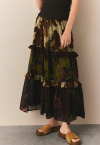 Fustă florală în mai multe straturi, de culoare verde închis, burgundy și crem, cu accente franjurate. Asortată cu sandale din suede maro, cu talpă joasă.