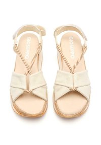 Sandalias de lona beige con un diseño de nudos, correas trenzadas y suela estilo espadrille texturizada. Presenta una plantilla acolchada y una correa ajustable en el tobillo.