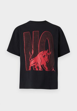 T-shirt noir avec un grand texte rouge "NON" et un graphisme de taureau rouge intégré aux lettres dans le dos.