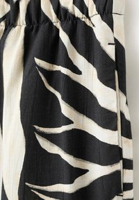 Tissu noir et beige avec motif abstrait de rayures façon zèbre et détail de taille élastiquée froncée.