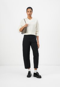 Pull en v crème avec ourlet côtelé, associé à un jean noir large taille haute et des chaussures à plateforme noires. Sac gris sur l'épaule.